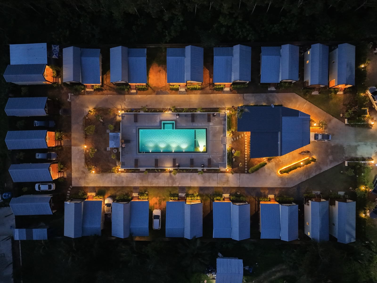 Top-down drone view of NaraRin Phuket at night — rows of cabins around the lit swimming pool